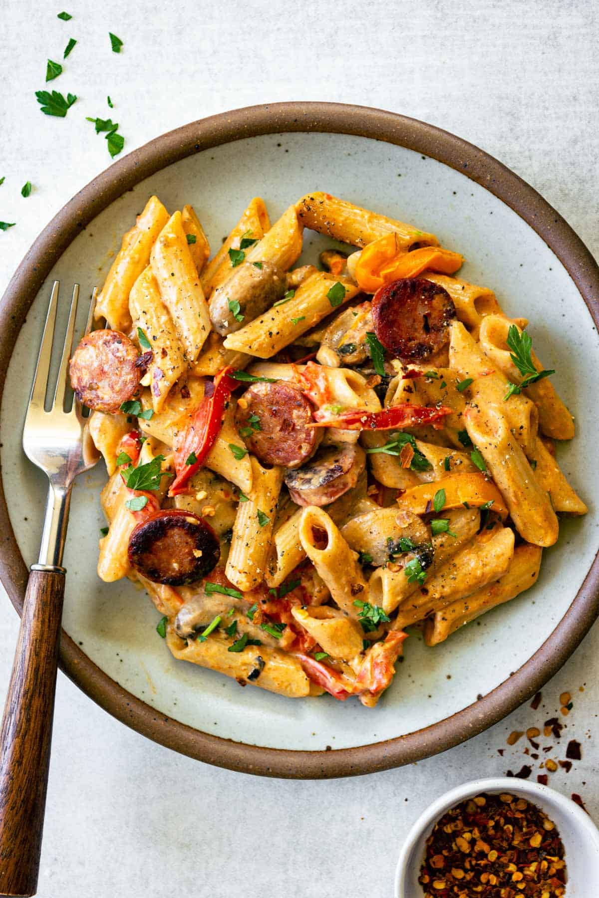 A plate of creamy pasta with sauasge and wooden handled fork.