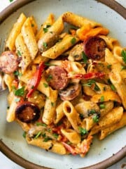 A plate of creamy pasta with sausage and wooden handled fork.