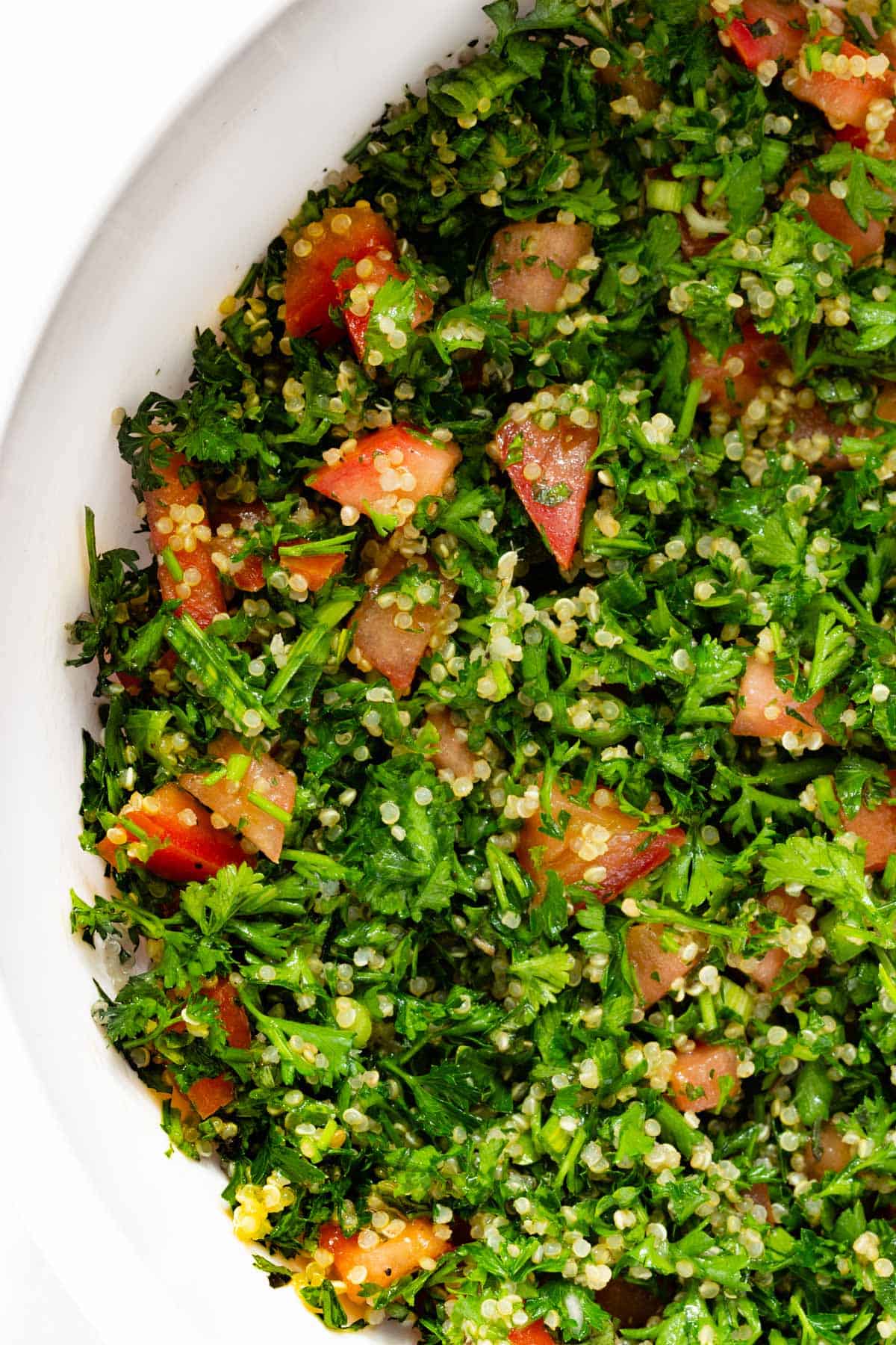 A close up of quinoa tabbouleh in a white serving bowl.