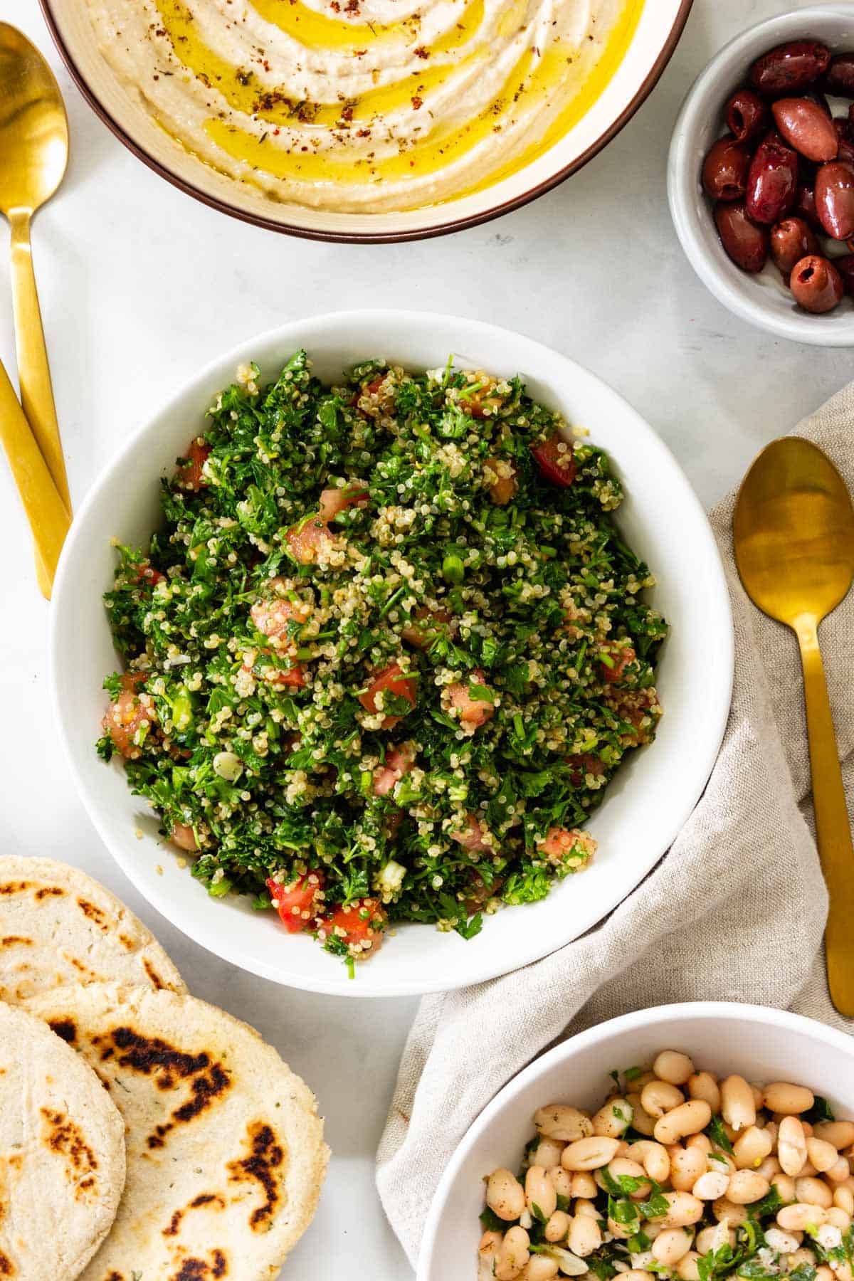 A bowl of quinoa tabbouleh sits on a table with other small plates of food.