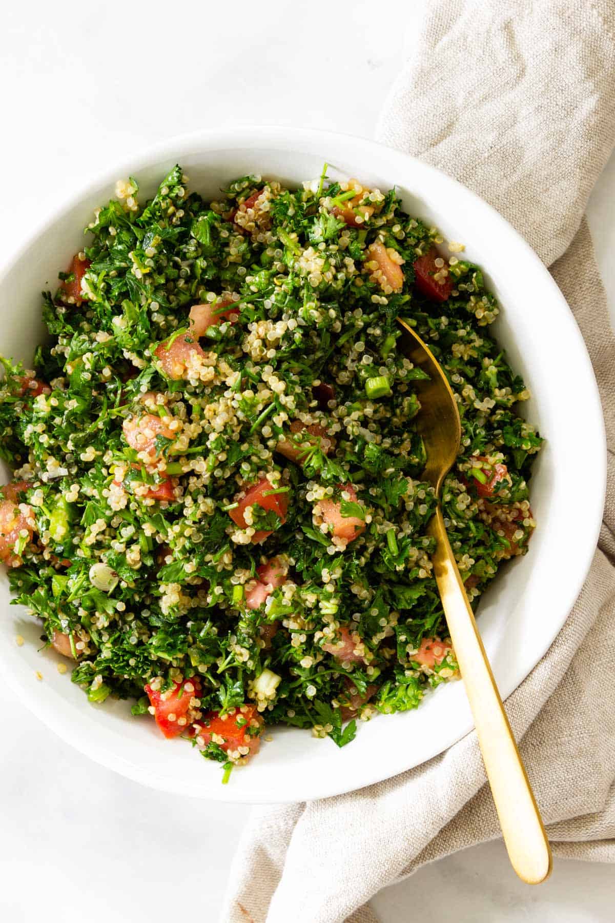 A white bowl of quinoa tabbouleh served with a gold spoon.