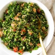A white bowl of quinoa tabbouleh served with a gold spoon.