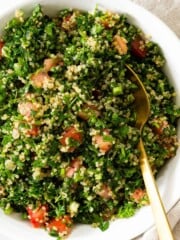 A white bowl of quinoa tabbouleh served with a gold spoon.