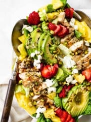 A strawberry chicken salad on a marble countertop next to a bowl of strawberries.