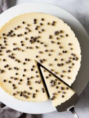 A cheesecake studded with mini chocolate chips is having a slice removed with a pie server.