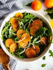 Arugula spinach salad topped with thinly sliced onions and mandarine slices.