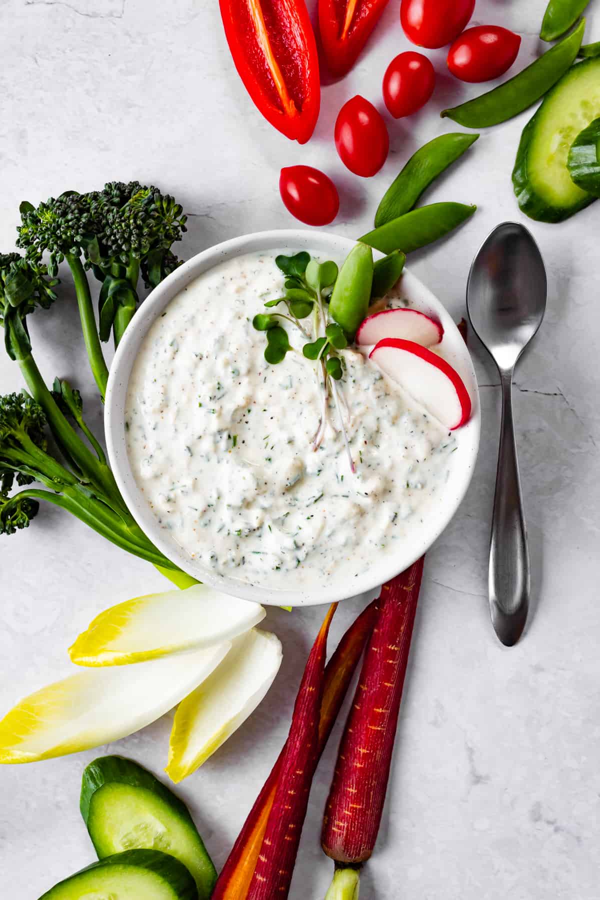 A bowl of dip with a variety of vegetables scattered about.