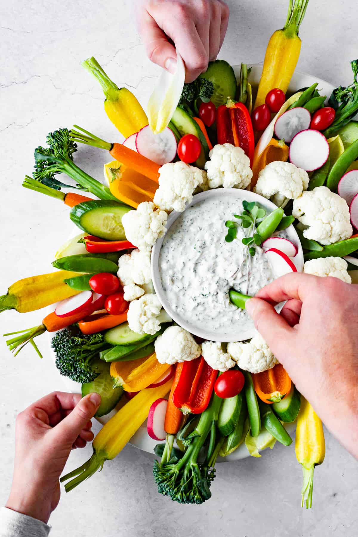 Several hands reach for veggies and dip.