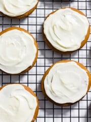 Gluten-free gingerbread cookies topped with cream cheese frosting on a cooling rack.
