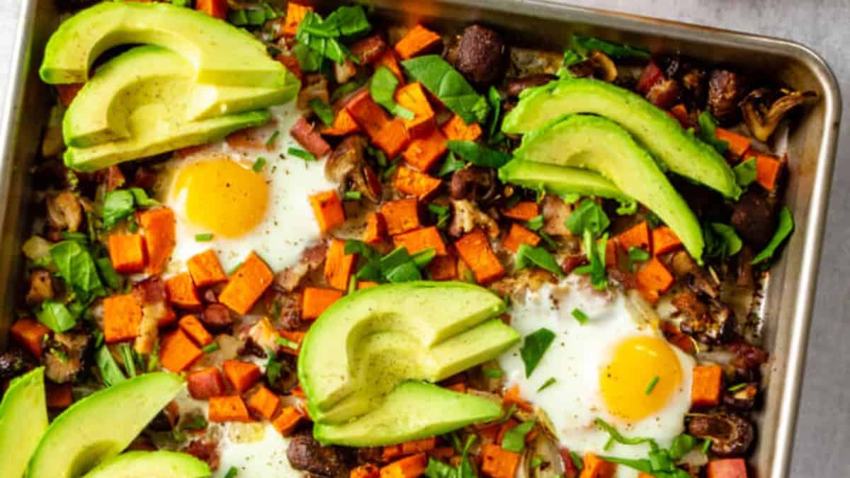 Sheet pan sheet potato hash is topped with baked eggs and avocado slices.