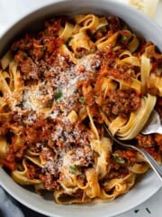 A bowl of pasta bolognese served with a chunk of parmesan.