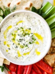 A bowl of homemade tzatziki surrounded by veggies and pita.