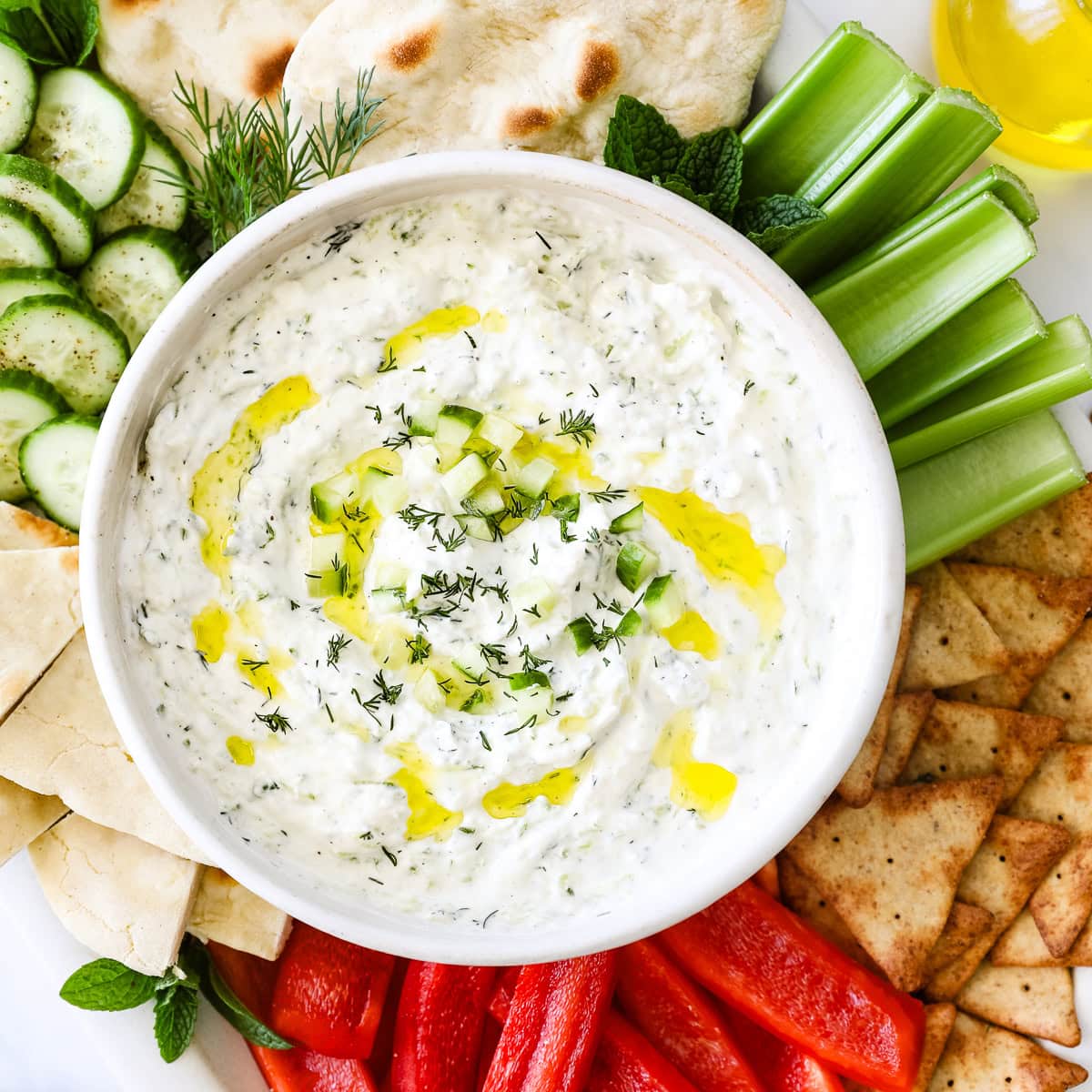 A bowl of homemade tzatziki surrounded by veggies and pita.