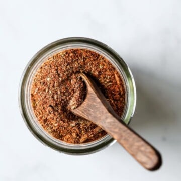 A little wooden spoon is scooped into a jar of homemade Cajun seasoning mix.