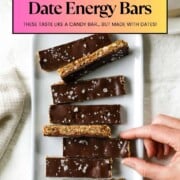 A hand reaches toward toward a plate of chocolate date energy bars next to a cup of tea.