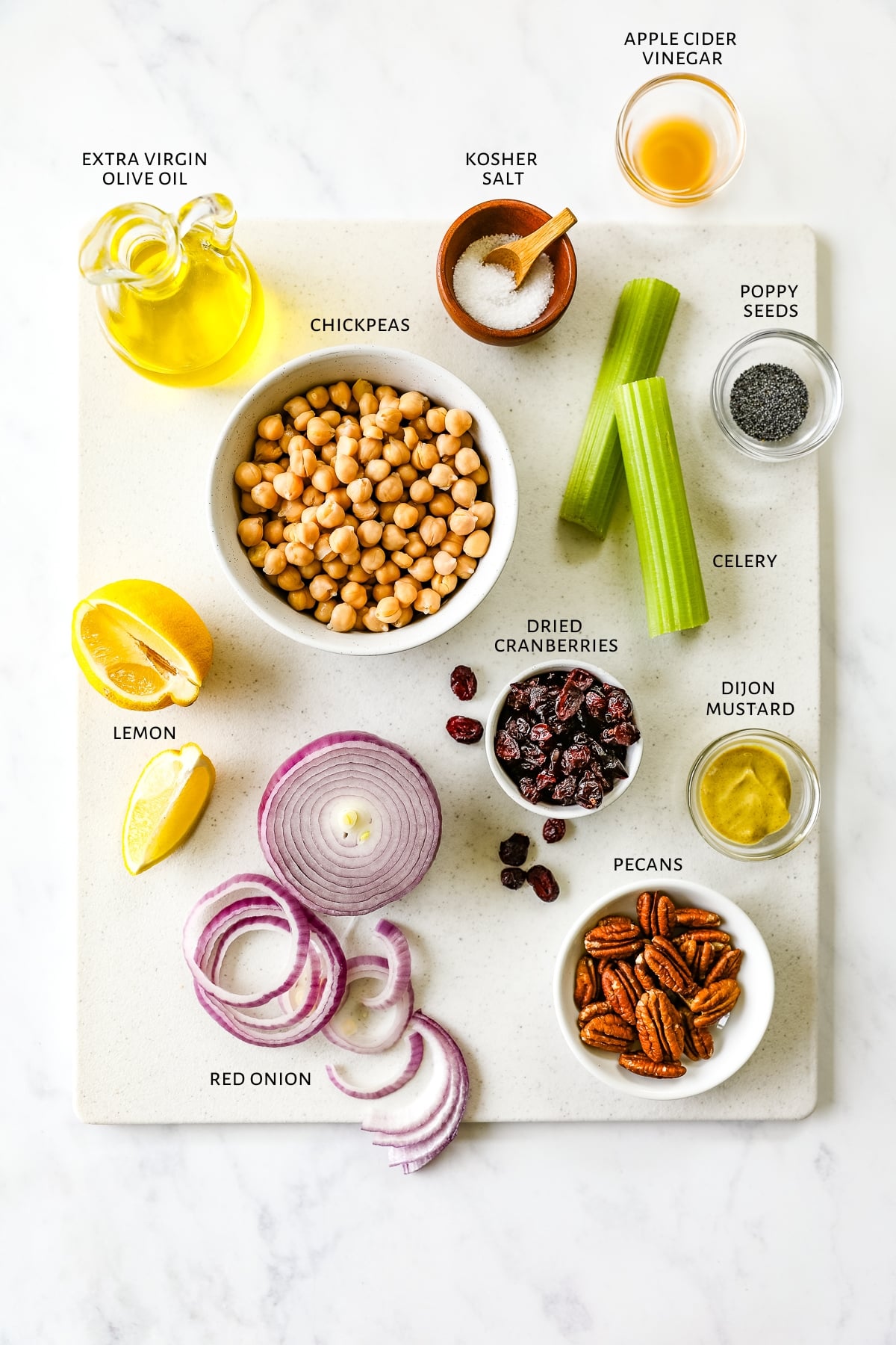 Ingredients for cranberry pecan chickpea salad are laid out on a marble countertop.